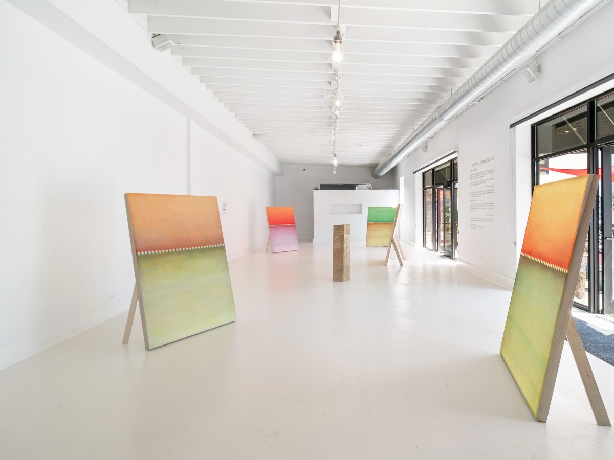 Installation view shows the long rectangular gallery with five large paintings on the floor via wooden stands and a wooden sculptural box in the center.