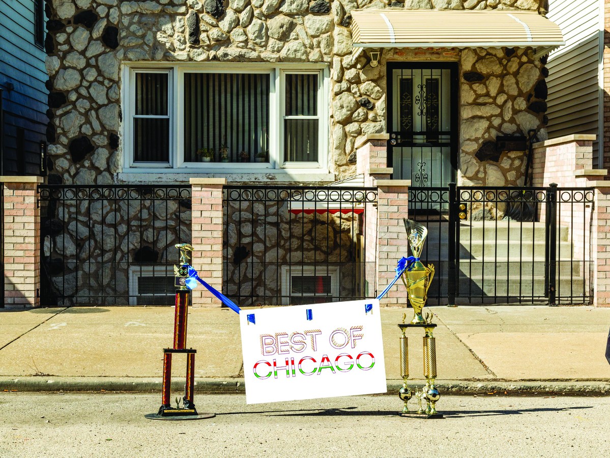 Best of Chicago Reader issue cover photo with a sign saying best of Chicago hanging from two trophies set on the ground dibs style in an empty parking space outside of a Chicago house