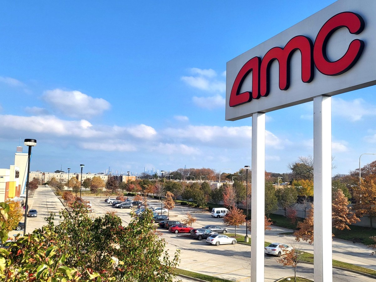 an AMC theater sign looms over a parking lot, with a cityscape far in the distance