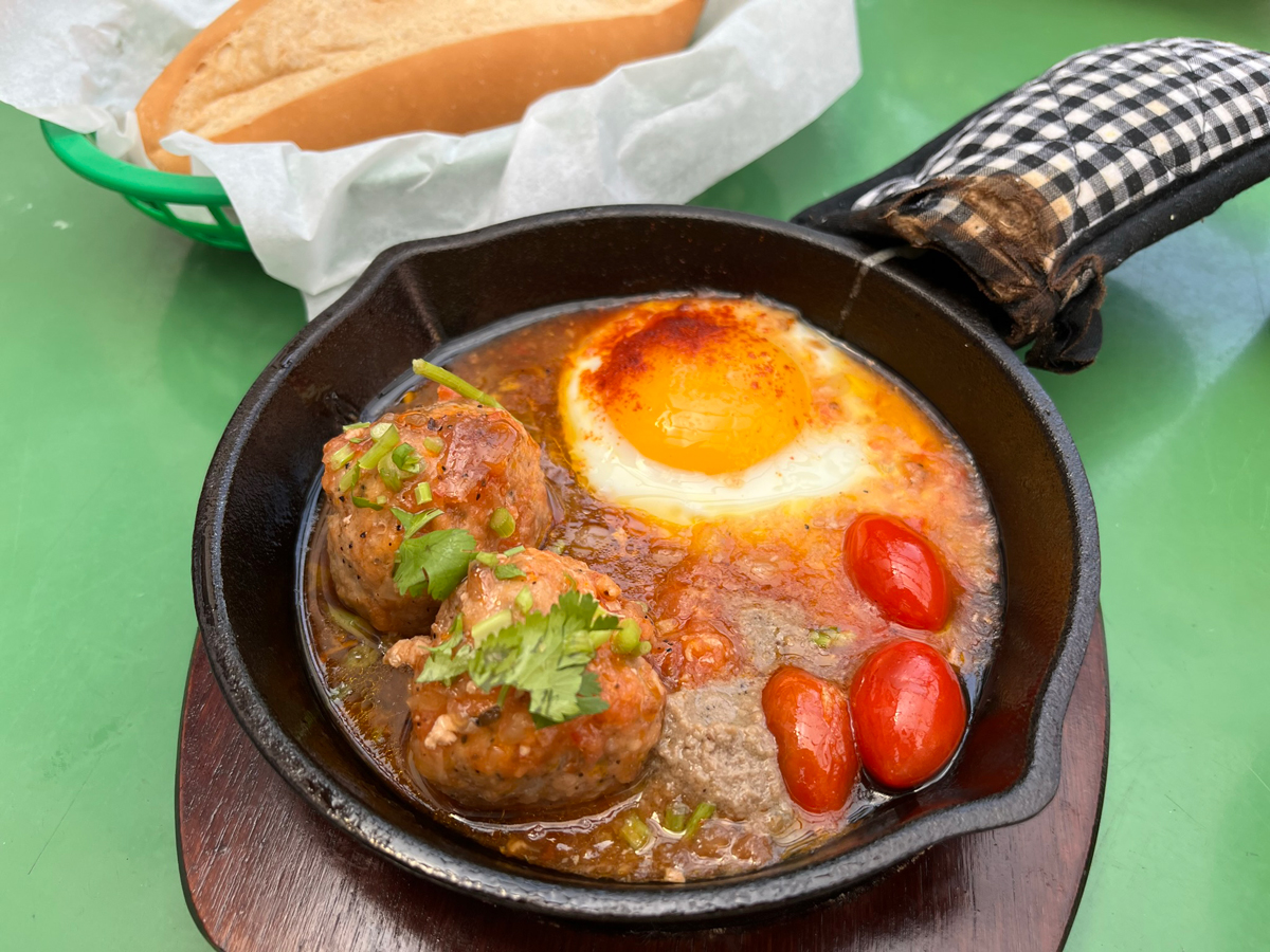 a skillet with meatballs, eggs, and cherry tomatoes