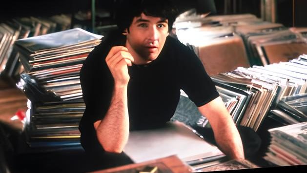 the book cover, with a still of John Cusack in High Fidelity above white and black text on an orange background