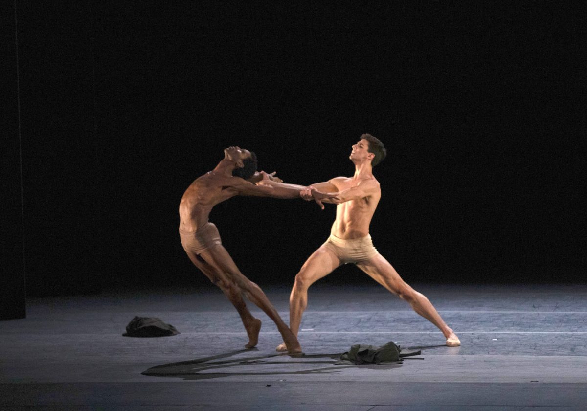 two men dancing onstage wearing flesh-tone briefs. The man on the left is Black and the man on the right is light-skinned.