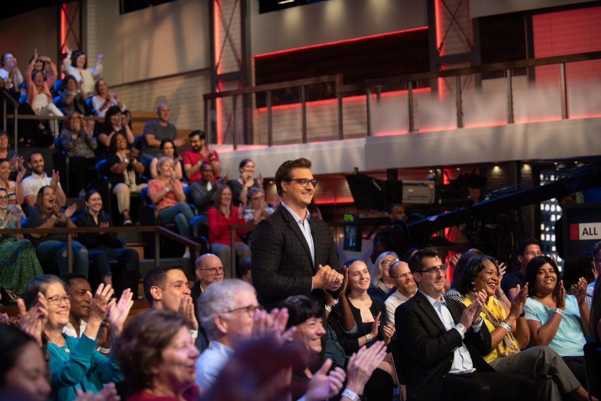 Chris Hayes stands within a seated audience surrounded by people