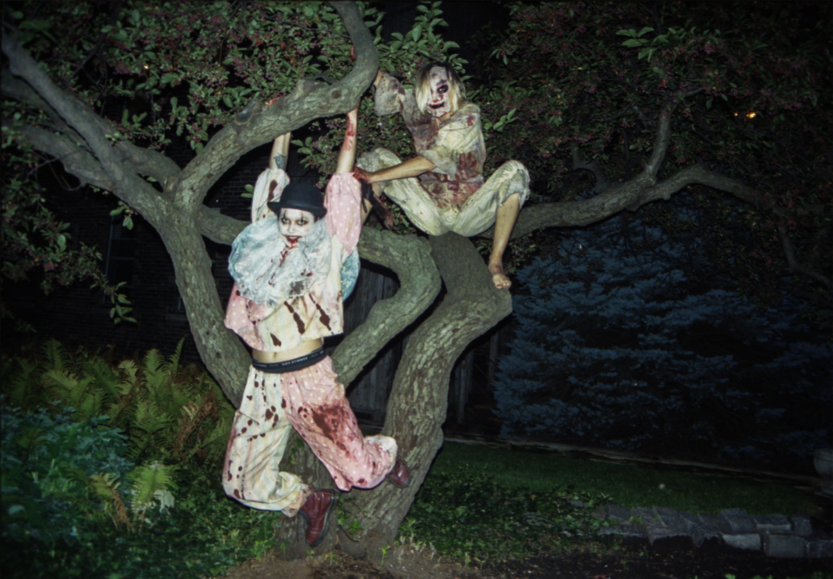 Two people in scary clown makeup and bloodstained clothing are pictured hanging out in a tree.