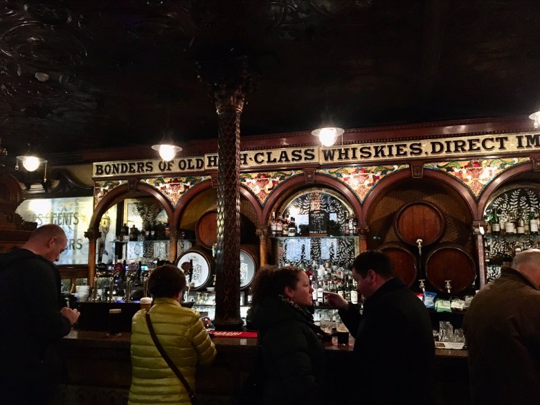 an elaborately carved wooden bar decorated with stained glass and tiles, dimly lit and crowded