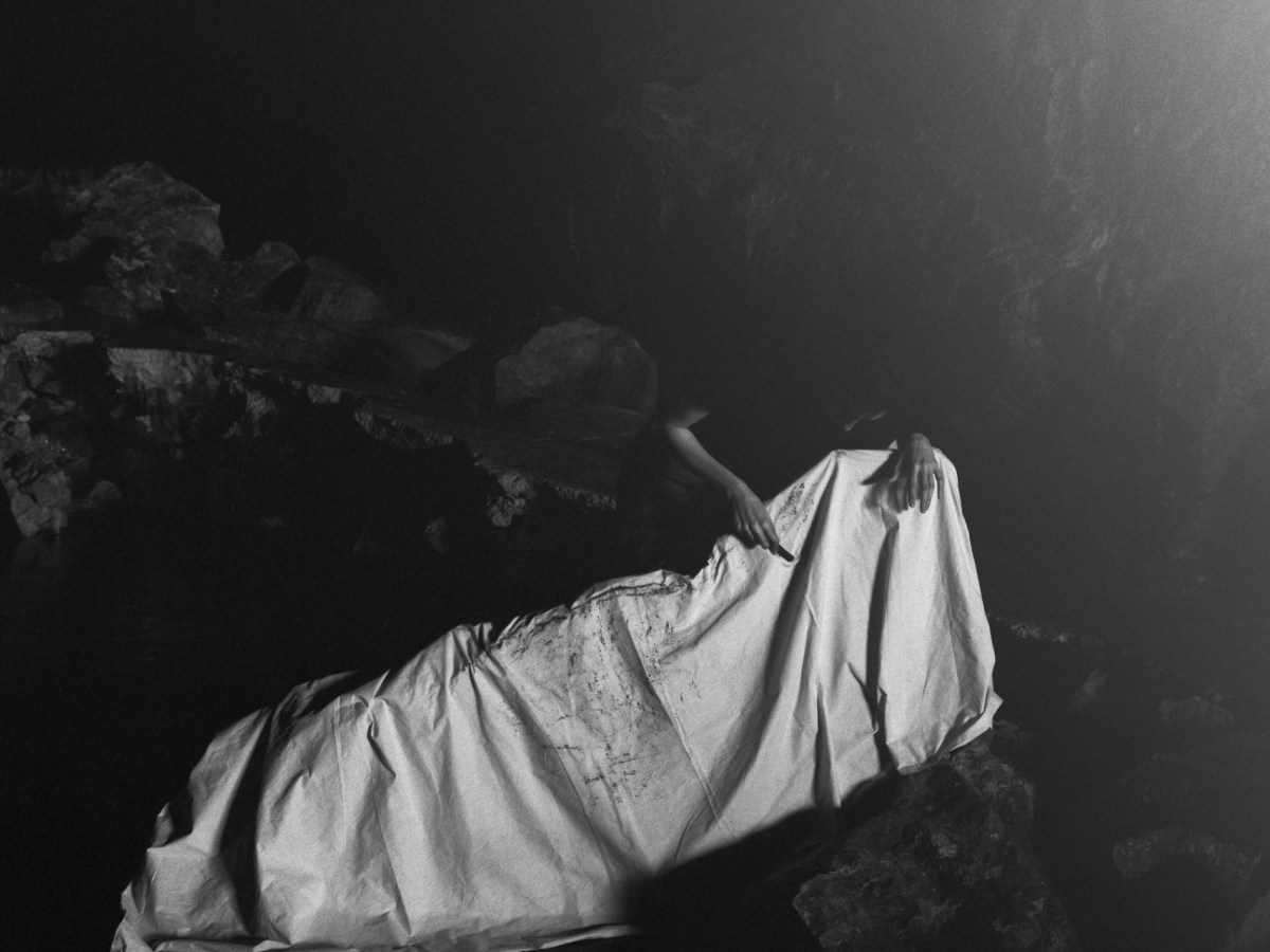 Black and white photo shows the artist in a dark cave, covering something with a large piece of white fabric.