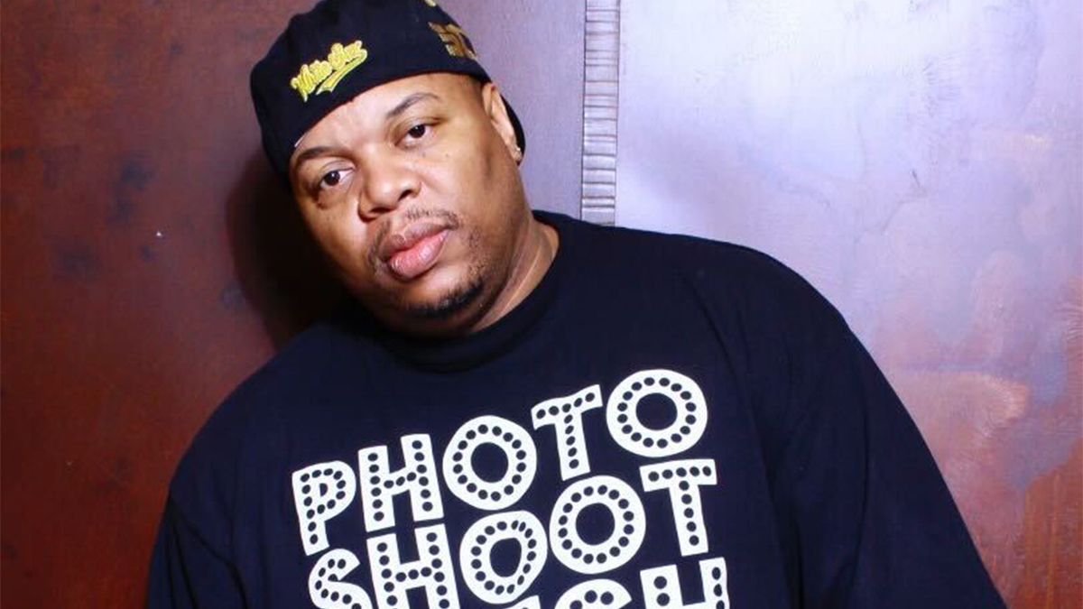 DJ Slugo wears a backward black ball cap and a black T-shirt that reads "photo shoot fresh"