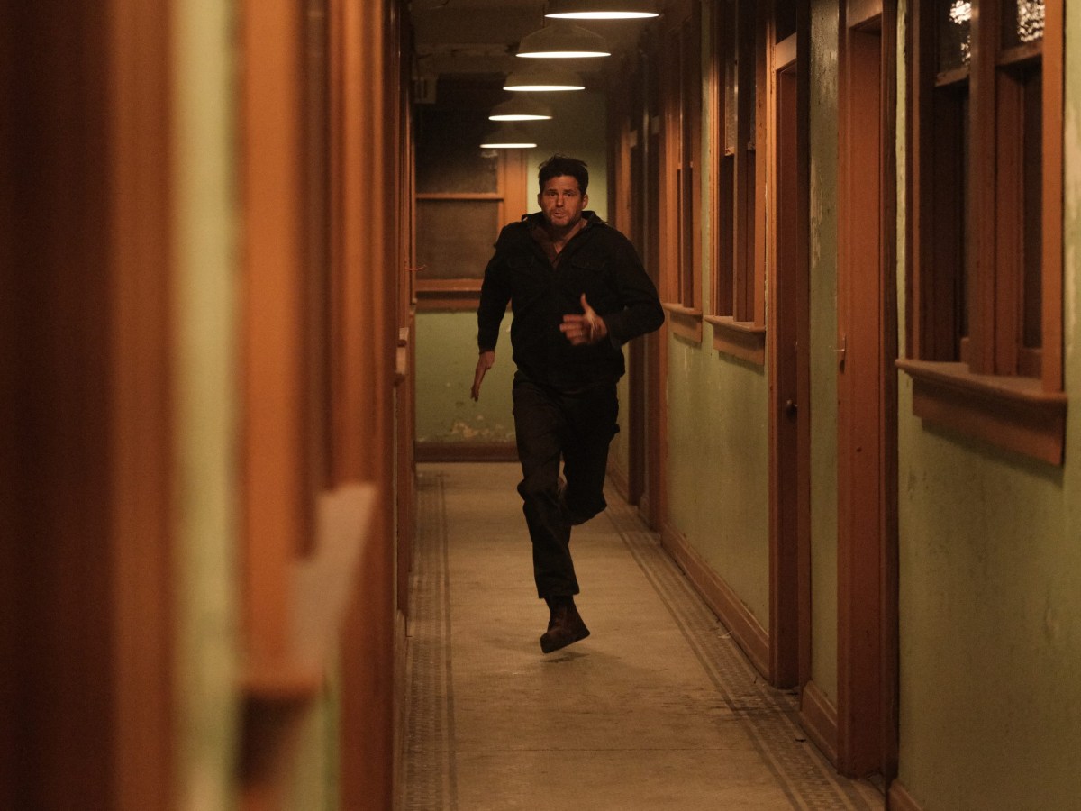 a white man runs down a dimly lit green and wood hallway