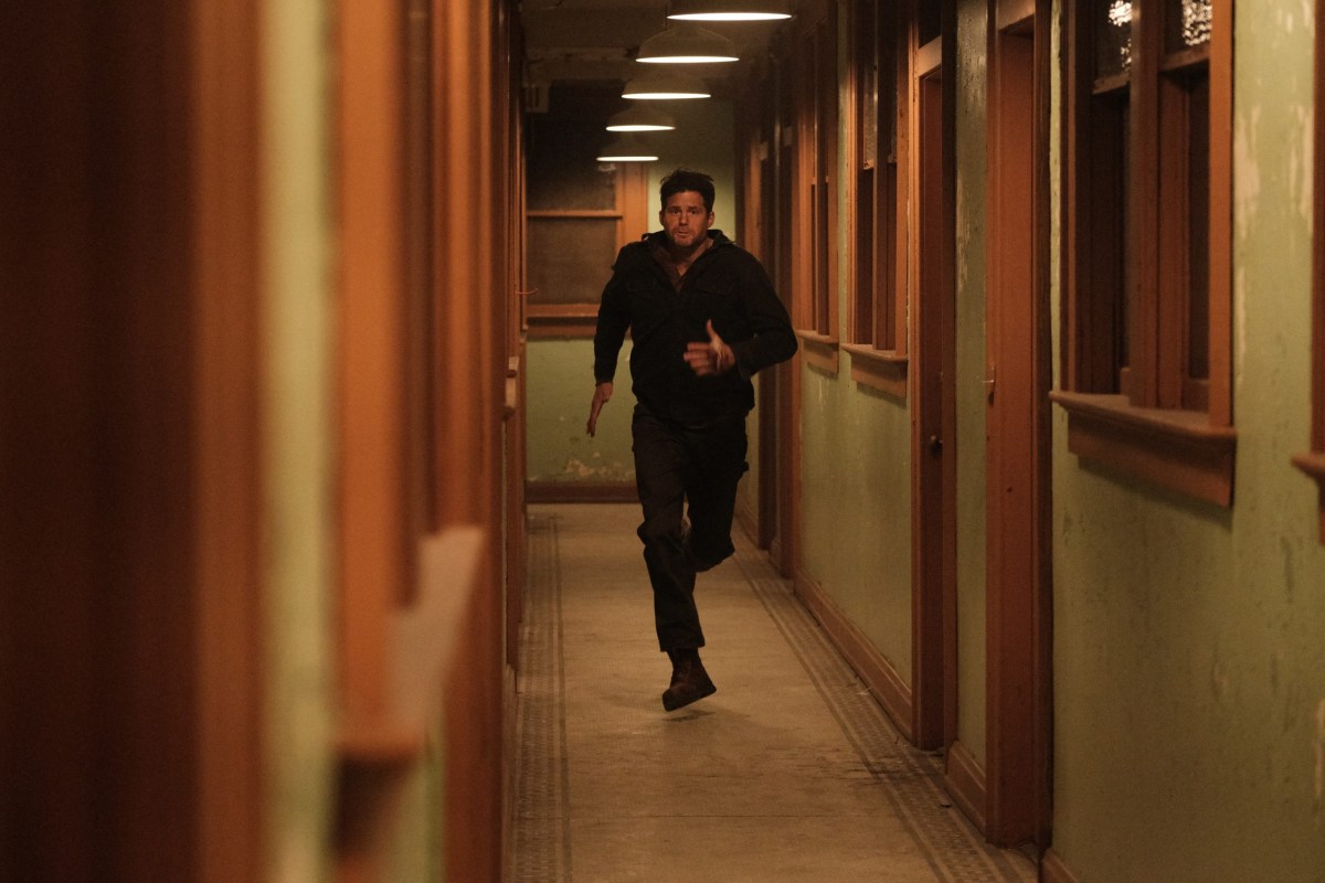 a white man runs down a dimly lit green and wood hallway