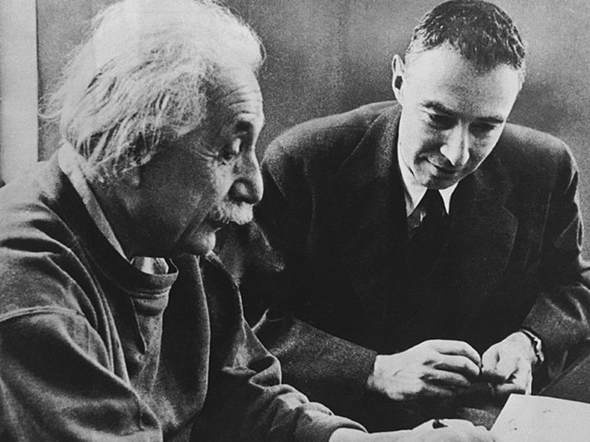 Black-and-white photo of Albert Einstein (left) and J. Robert Oppenheimer seated and looking at a document.