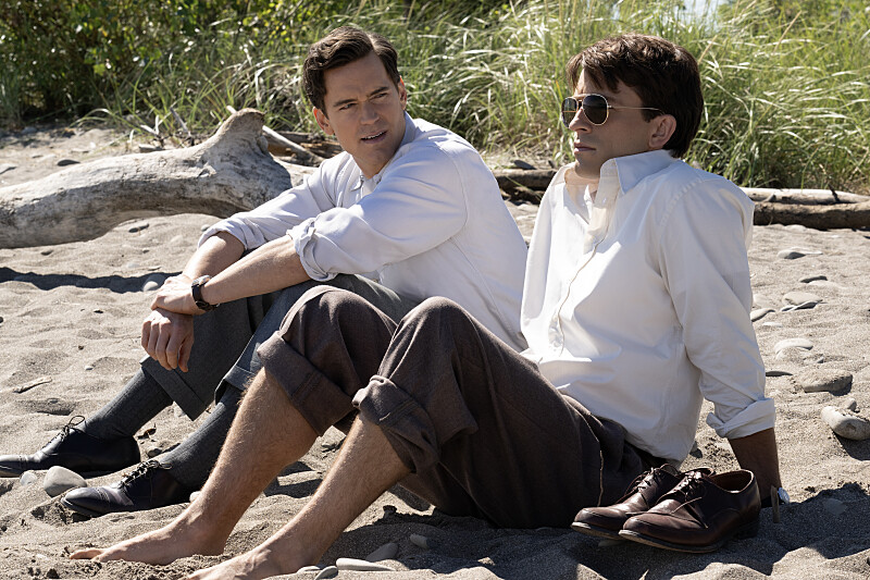 two white men sit on a sandy beach in work clothes