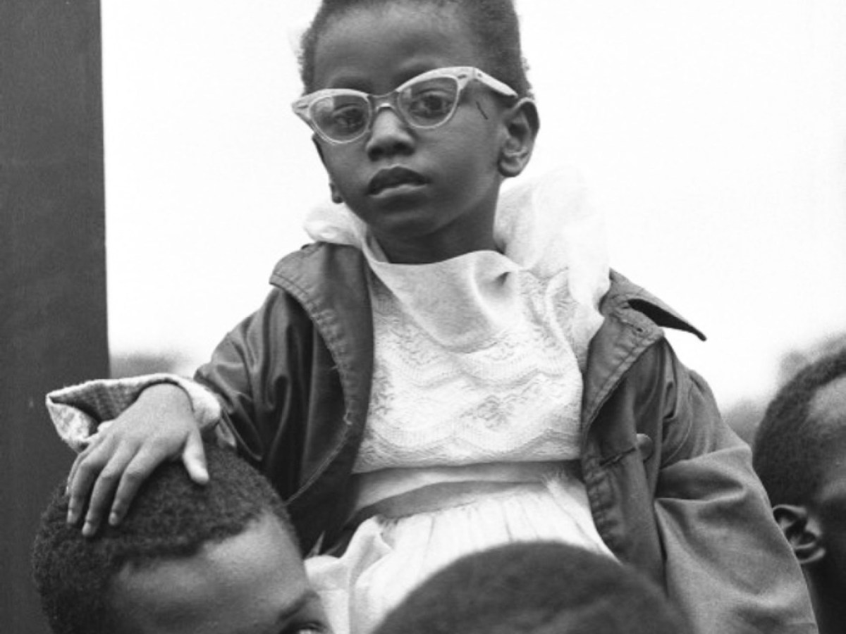 Cover image is a black and white photograph showing a small Black girl sitting on the shoulders of a young Black man. Other people can be seen in the back and foregrounds. The subjects are dressed in the clothes of the 1960s. The title is in bright blue text.
