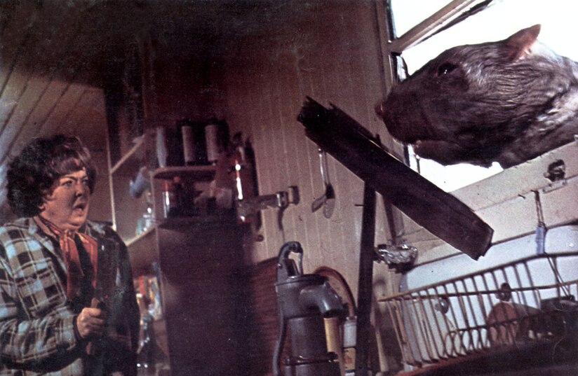 a giant rat head busts through a window near a scared woman