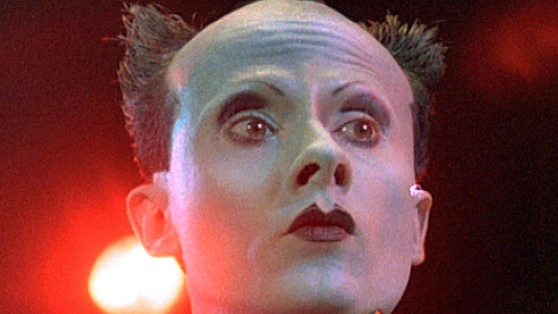 a face sharply painted white, with thin eyebrows, small pointed lips, and an odd half-bald haircut