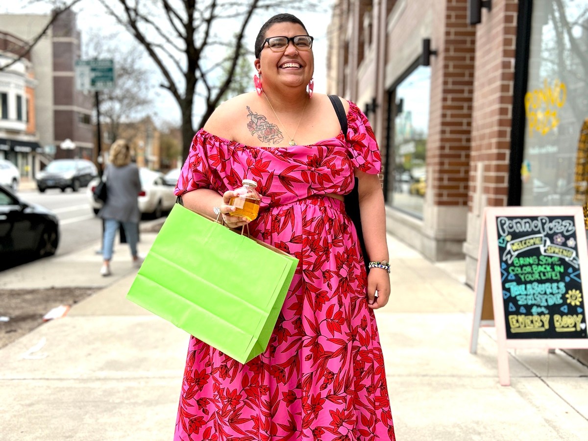 Alexis P. Morgan stands on the sidewalk outside Ponnopozz store in Ravenswood, Chicago. Morgan wears a hot pink cropped off the shoulder top with matching hot pink maxi skirt and is holding a lime green bag