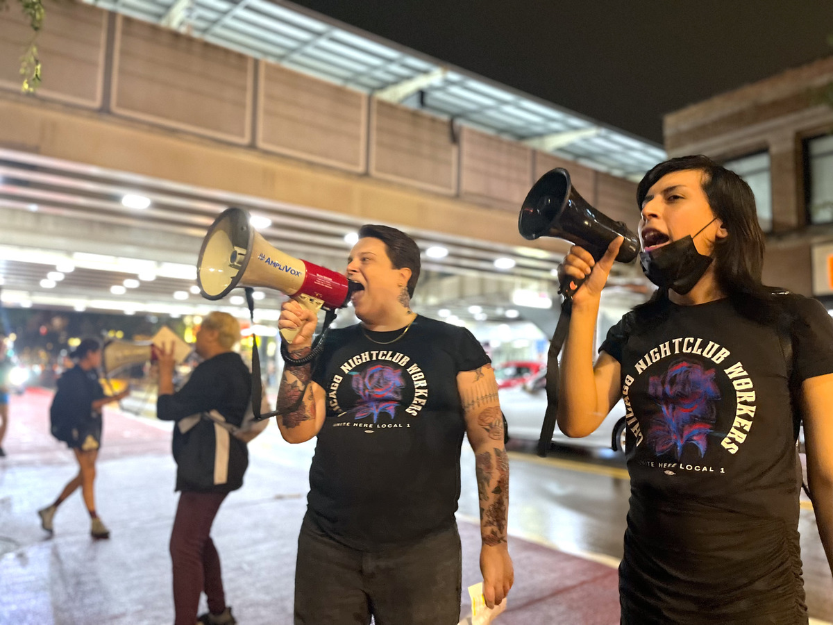 Two protestors holding megaphones near their mouths at the Berlin Nightclub strike rally in August 2023. The Belmont Red Line el stop is visible in the background