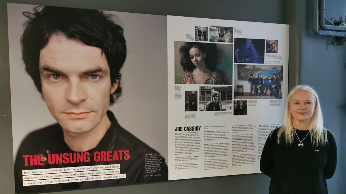 Joe Cassidy's sister, Frances Macklin, with a wall display at the Oh Yeah Music Centre in Belfast that includes a portrait of Cassidy by Paul Elledge