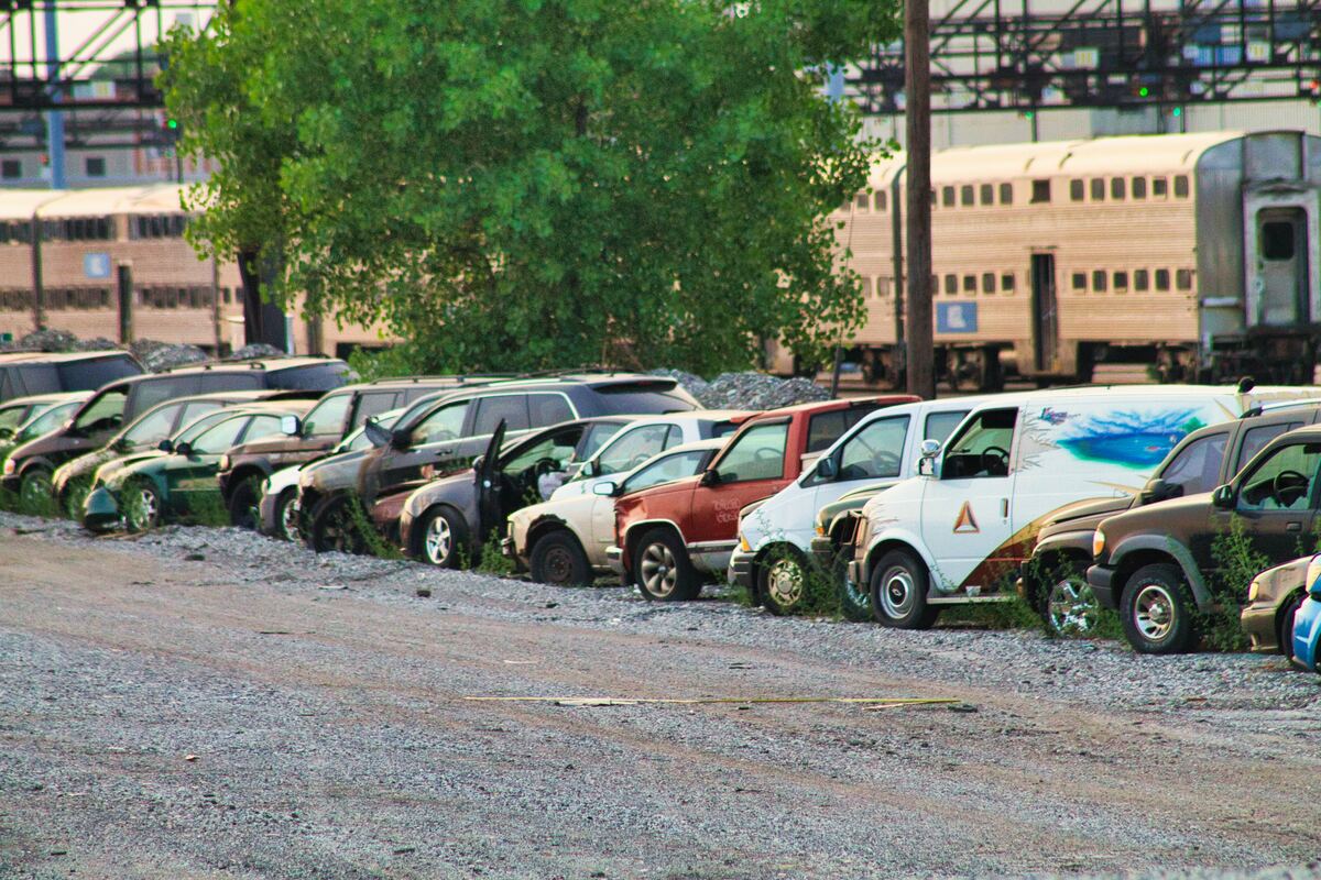 a row of cars parked in one of the city of chicago's auto tow pounds an outdoor lot near a railway. a metra commuter train is in the background