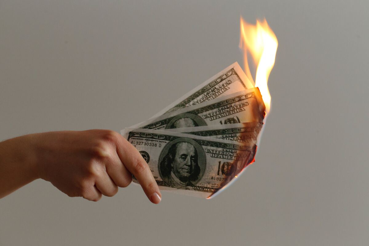 photo of a hand holding money, the cash is on fire