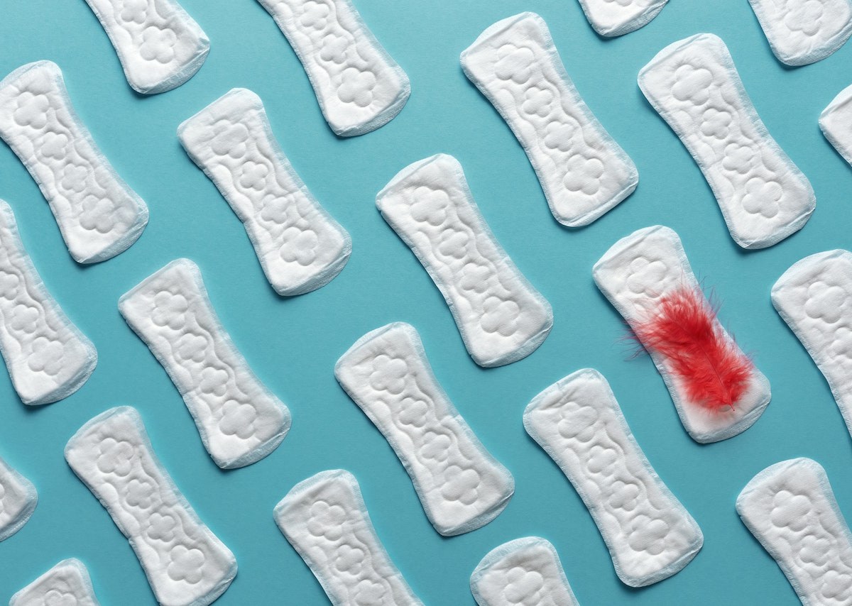 white sanitary napkins on a teal background. there is a clump of red feathers on one of the napkins