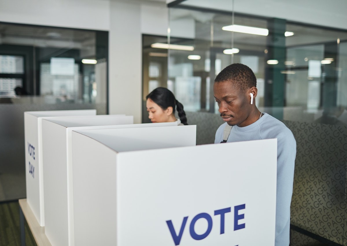 A Black man and an Asian American woman stand at individual voting booths