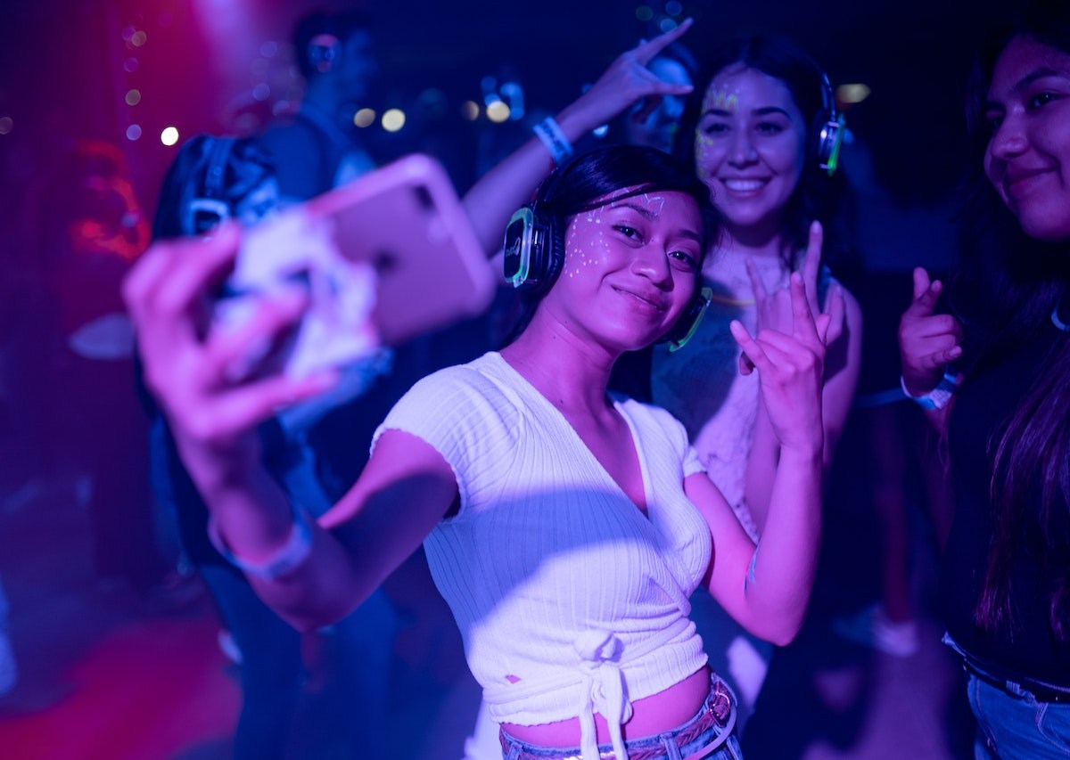 a woman wearing a white tshirt takes a selfie with her friends in a nightclub