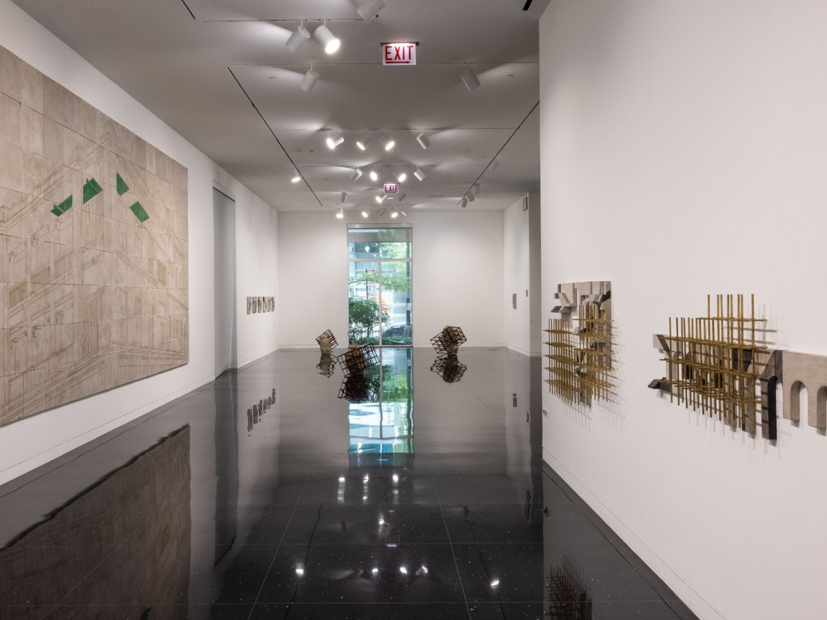 a large 2D work hangs on the left hand gallery wall, and sculptural works on the right wall. The center of the image shows the gallery's gleaming black floor, with floor sculptures in the distance. A window is at the far end, with greenery seen through it.