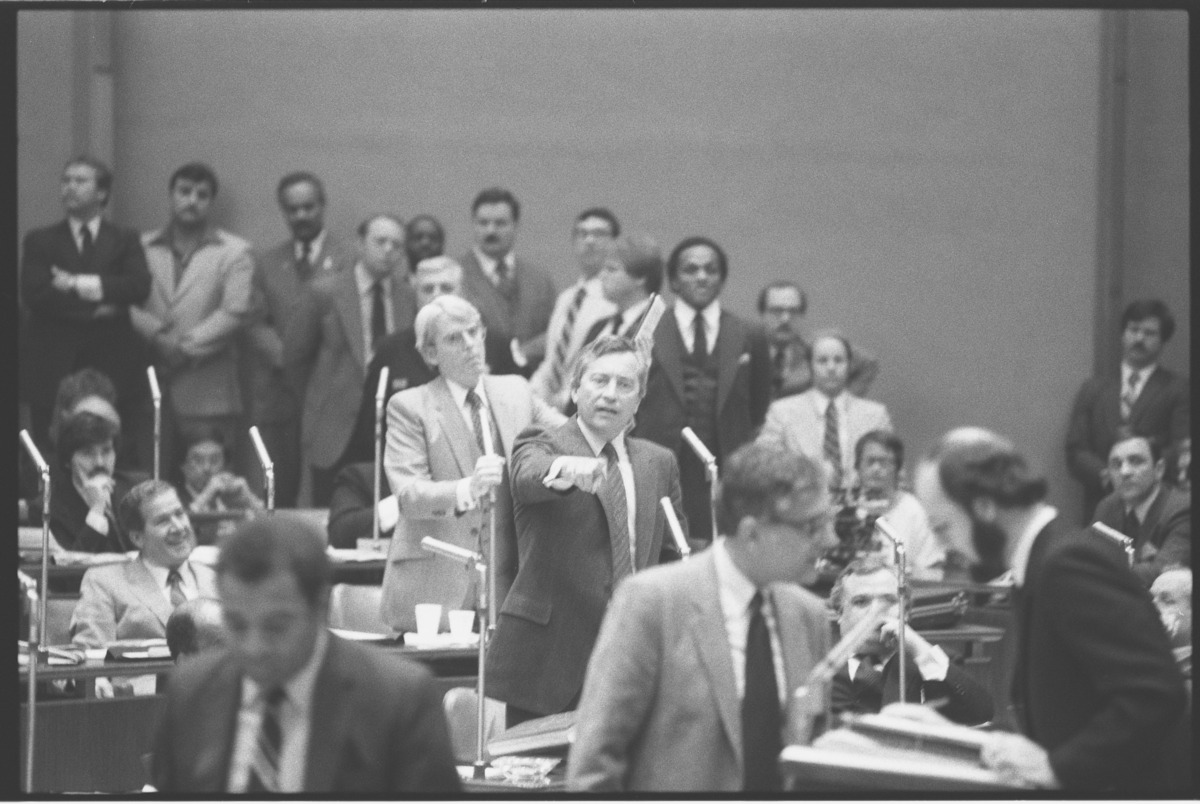 1983 photo: Alderman Edward Vrdolyak standing, center gesturing during a meeting of the Chicago City Council with Mayor Harold Washington, as Alderman Edward M. Burke stands behind him.
